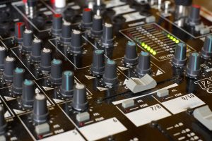 Ein Mischpult in Nahaufnahme mit zahlreichen Schaltern und Reglern sowie Leuchtanzeigen.