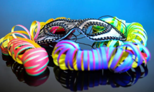 Eine mit Strasssteinen besetzte Maske liegt auf bunten Luftschlangen.